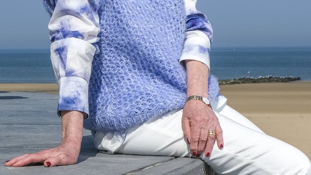 Greta Vandeborne, in het blauw en wit gekleed, poseert voor een zicht op het strand en de zee