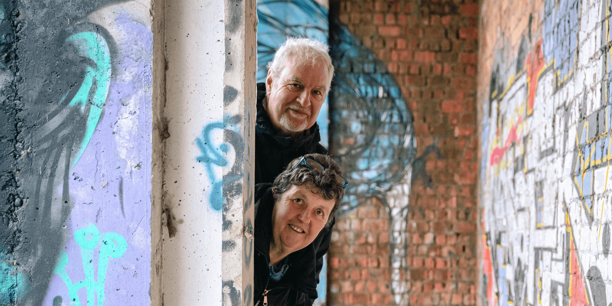 Een man en een vrouw kijken om de hoek van een muur in de hotelruïne van het Vrijbroekpark.