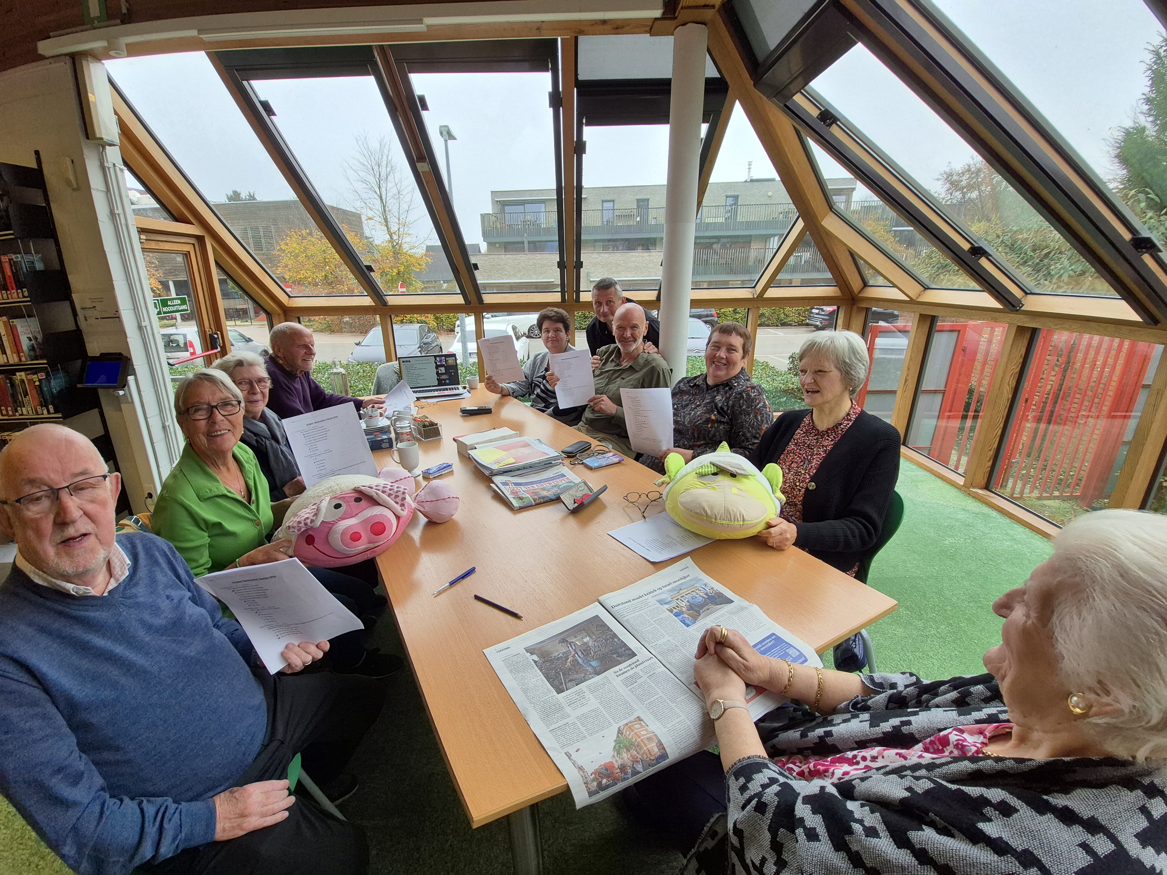 Mensen zitten aan tafel met een tas koffie of thee en krant, een prijzen van een Quiz.
