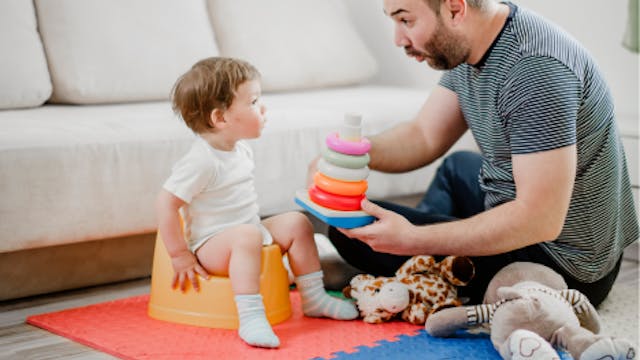 papa op de grond met speelgoed bij zijn zoon op het potje