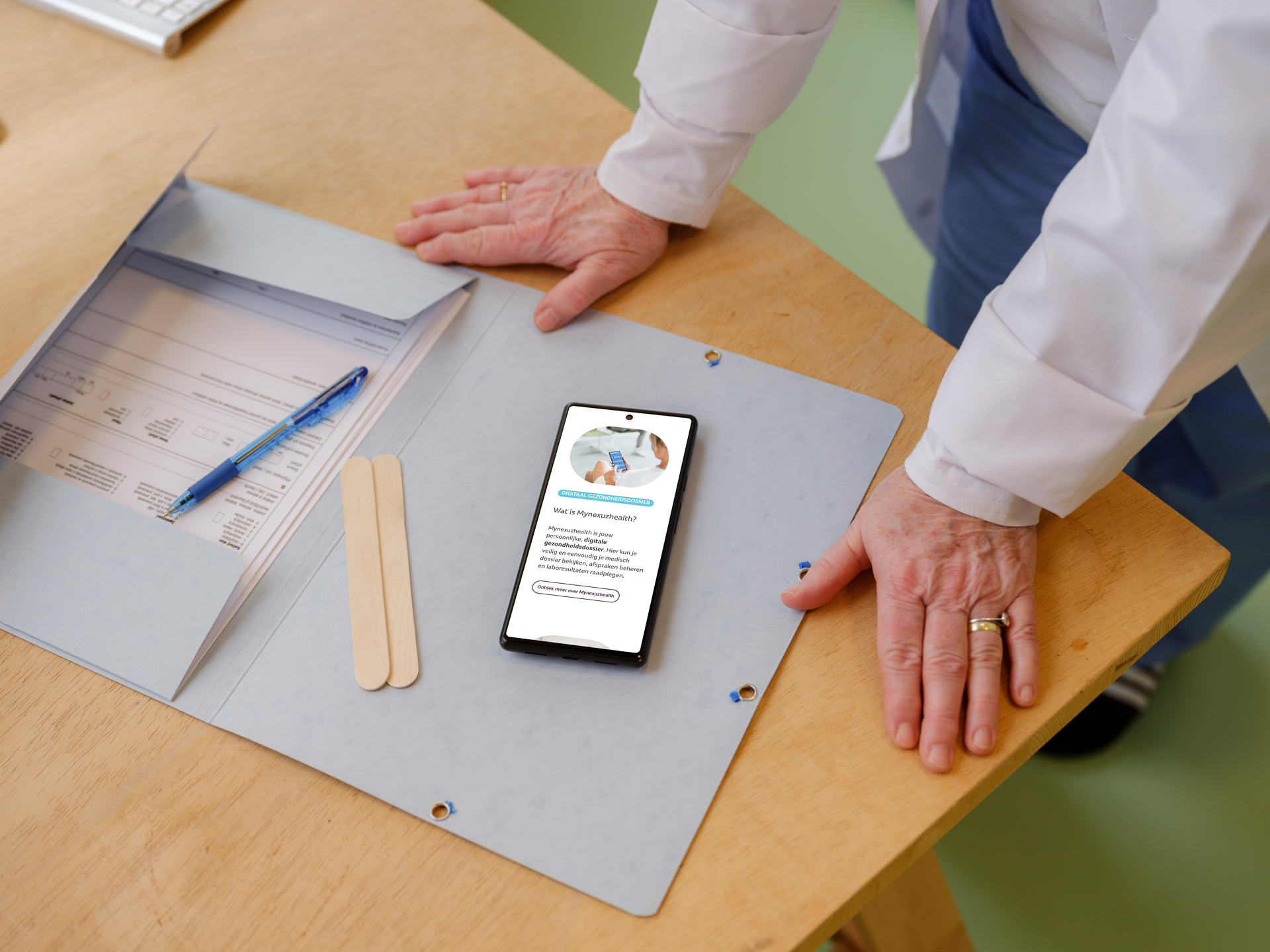Persoon die buigt over map op tafel en smartphone waar mynexuzhealth op getoond wordt