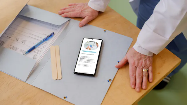 Persoon die buigt over map op tafel en smartphone waar mynexuzhealth op getoond wordt