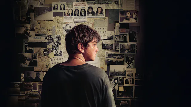 Een man kijkt naar een muur vol foto's en kaarten, die verbanden tonen.