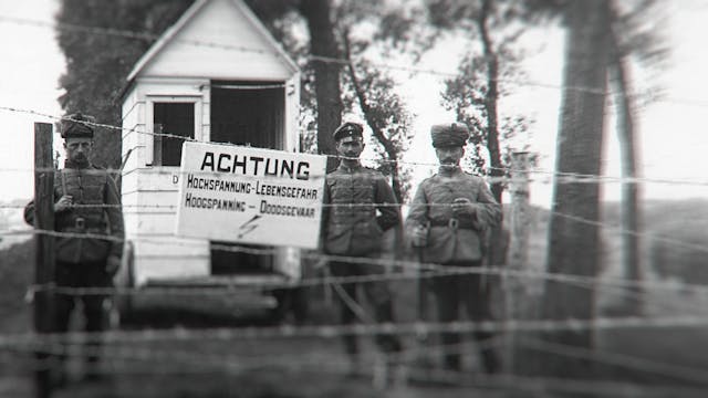 Zwart-witfoto van drie soldaten bij een wachthuisje met een bord "Achtung" en prikkeldraad.