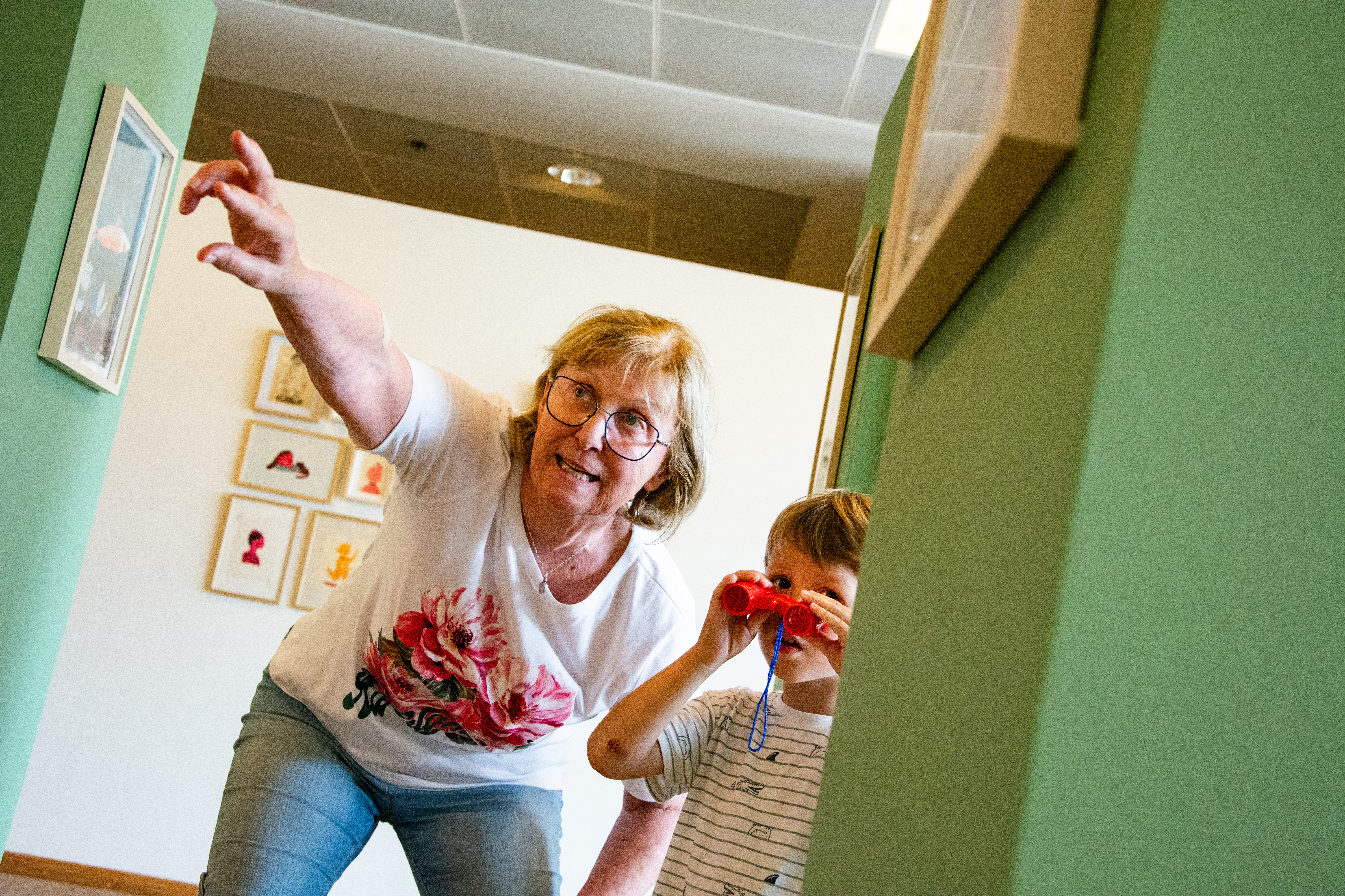 Een oma wijst en een kleinkind kijkt door een kleine rode verrekijker 