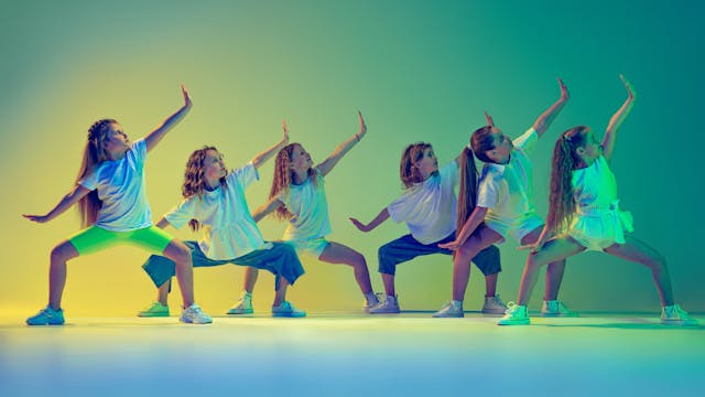 Group of children, little girls in sportive casual style clothes dancing in choreography class isolated on green background in yellow neon light. Concept of music, fashion, art