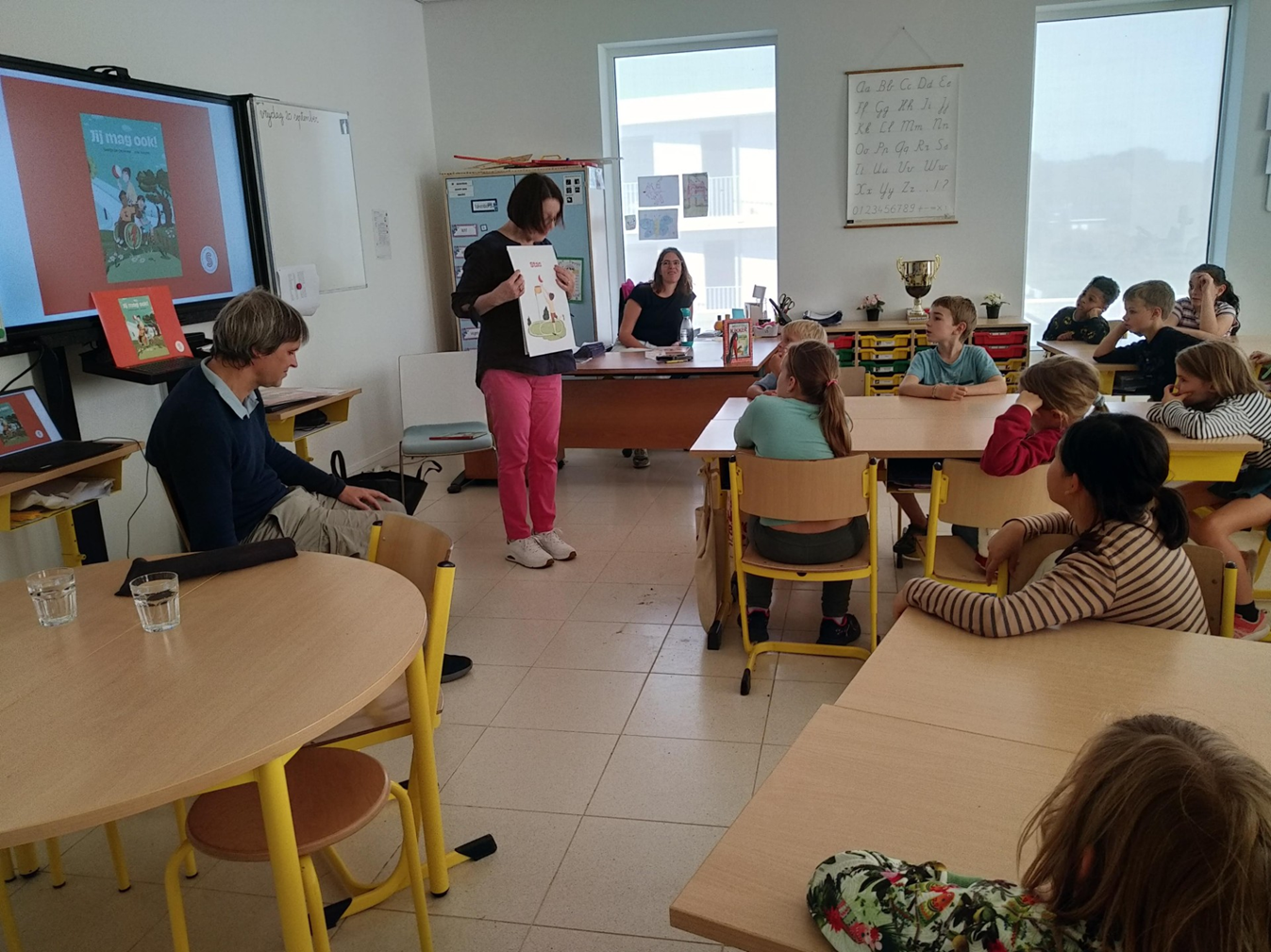 Een klaslokaal met kinderen die luisteren naar een presentatie over een boek.
