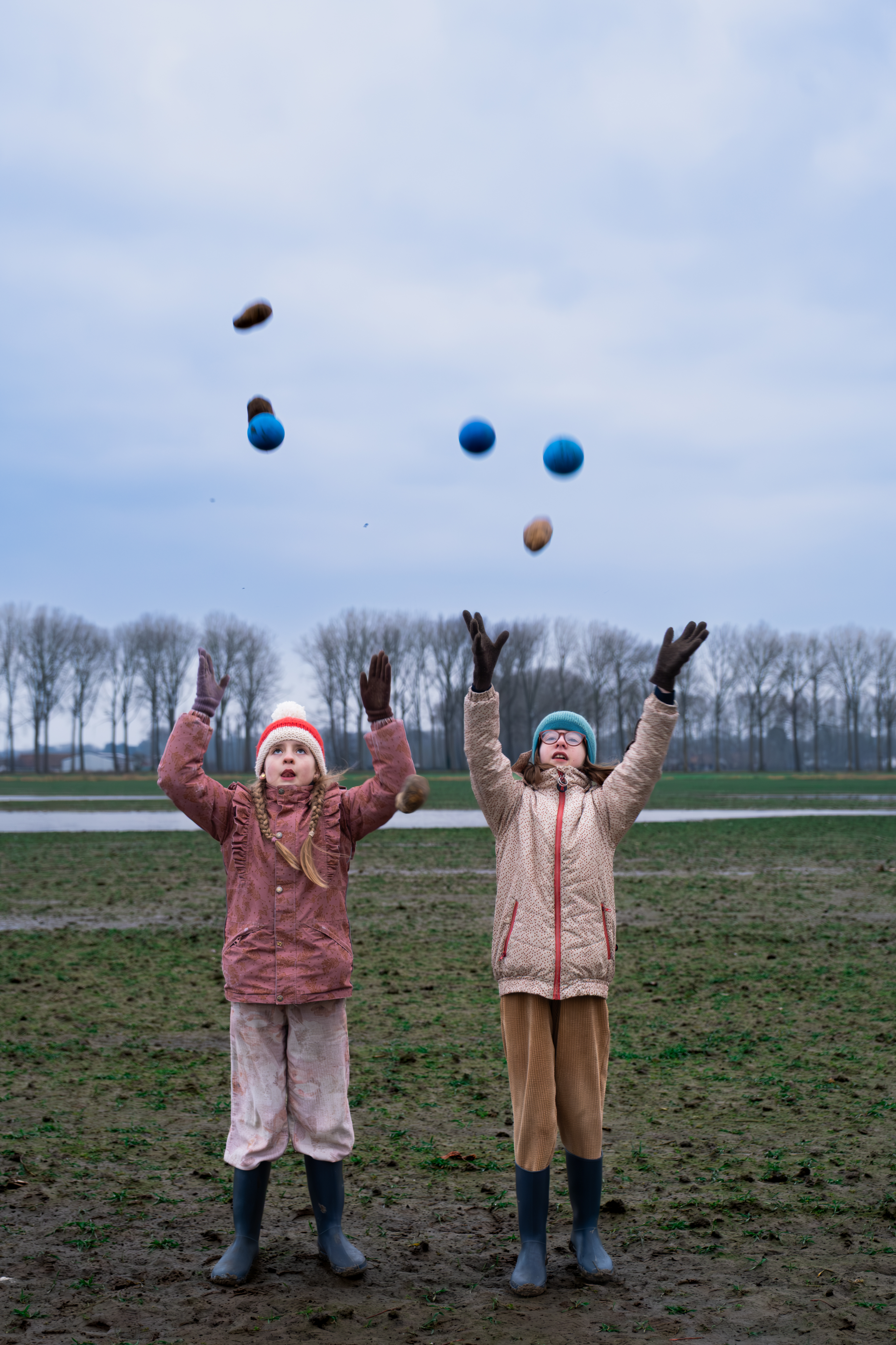 Twee meisjes met botten aan gooien ballen en pattatten in de lucht op een patattenveld