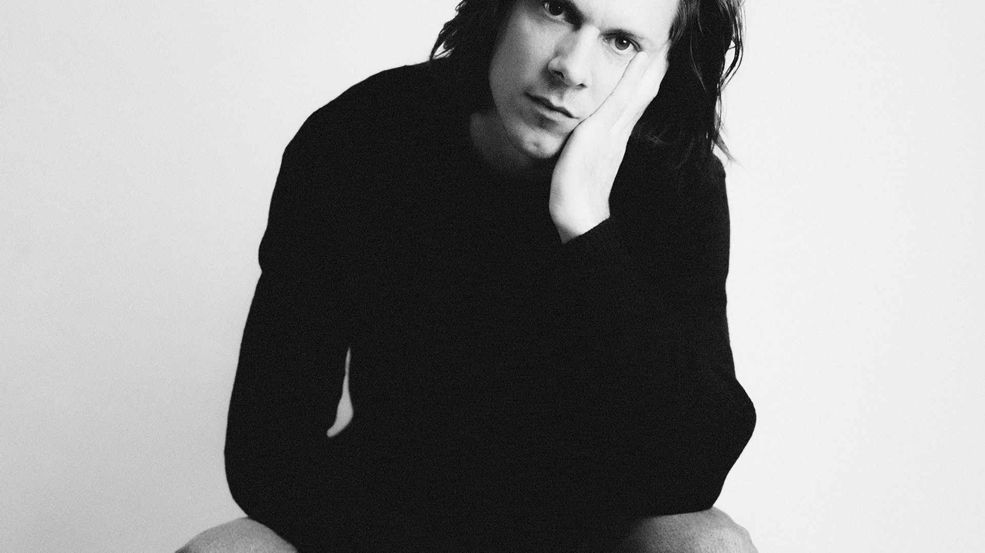 Zwart-witfoto van The Bony King of Nowhere zittend op stoel met hand tegen gezicht.