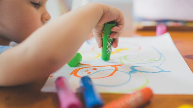 Een kleuter kribbelt met wasco's op een papier.