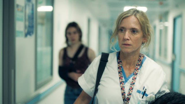 Hoofdverpleegkundige Lucy wandelt piekerend door de ziekenhuisgang.