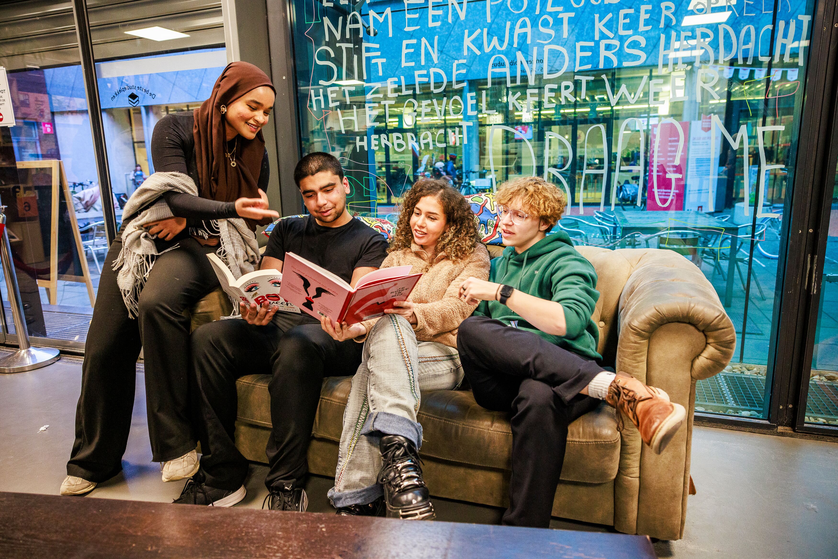 Vier jongeren zitten in een sofa in de jongerenbib van bibliotheek Permeke. Twee houden een boek vast.