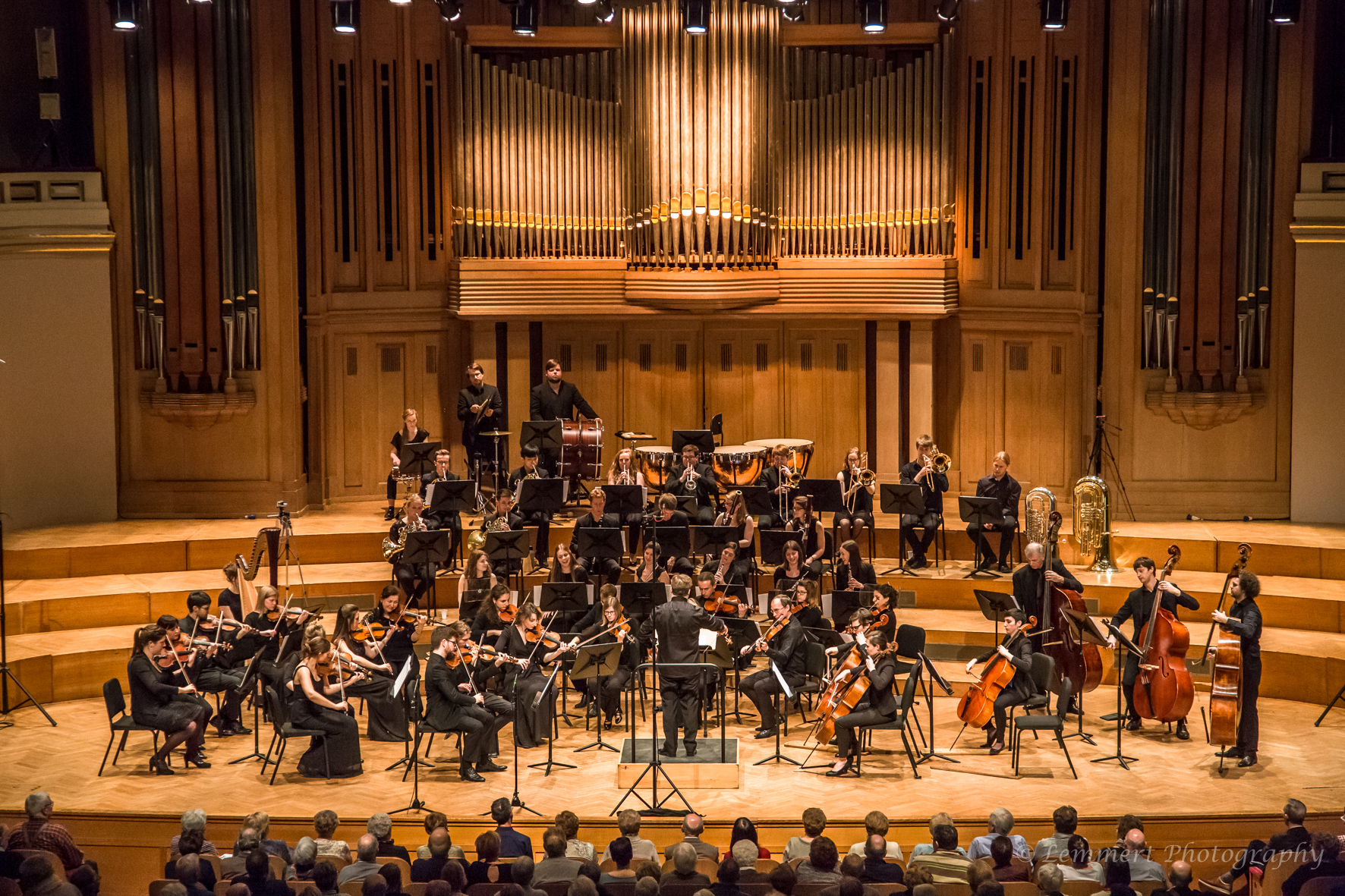 Een orkest speelt op een podium met een grote orgel achtergrond.