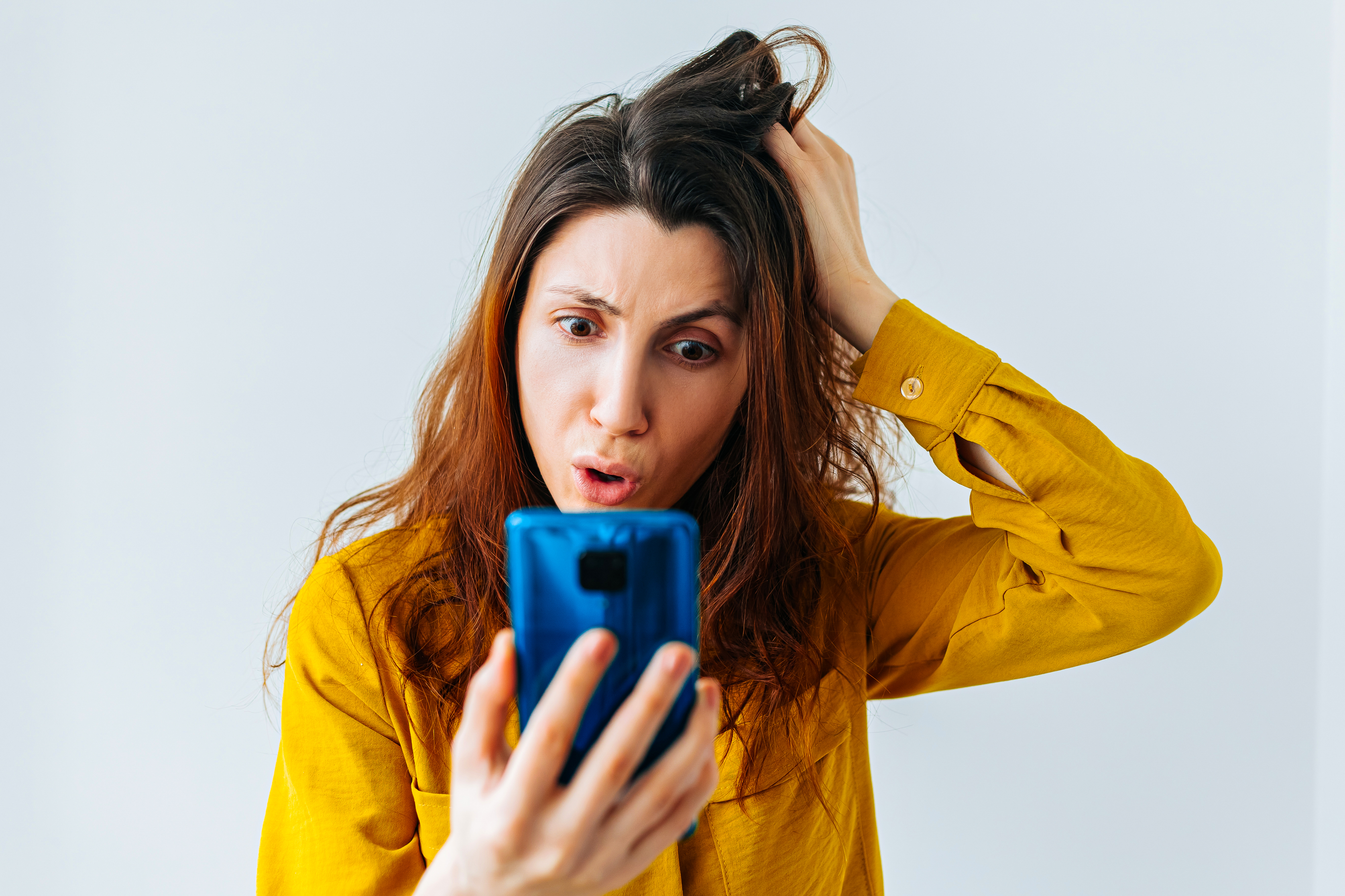 Persoon krabt zich in het haar bij het kijken naar de gsm.