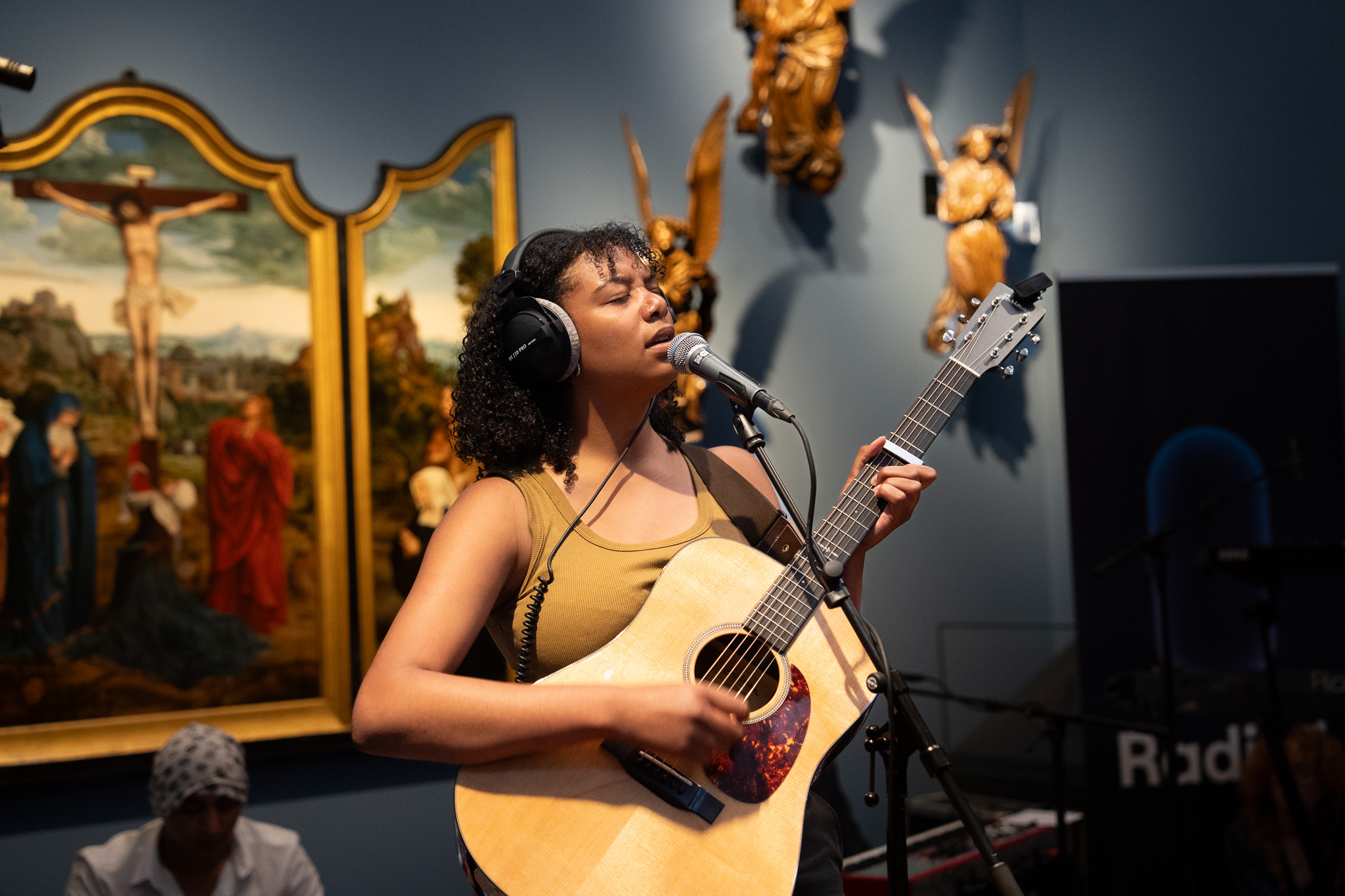 Een jonge vrouw zingt en speelt gitaar in een museumzaal.