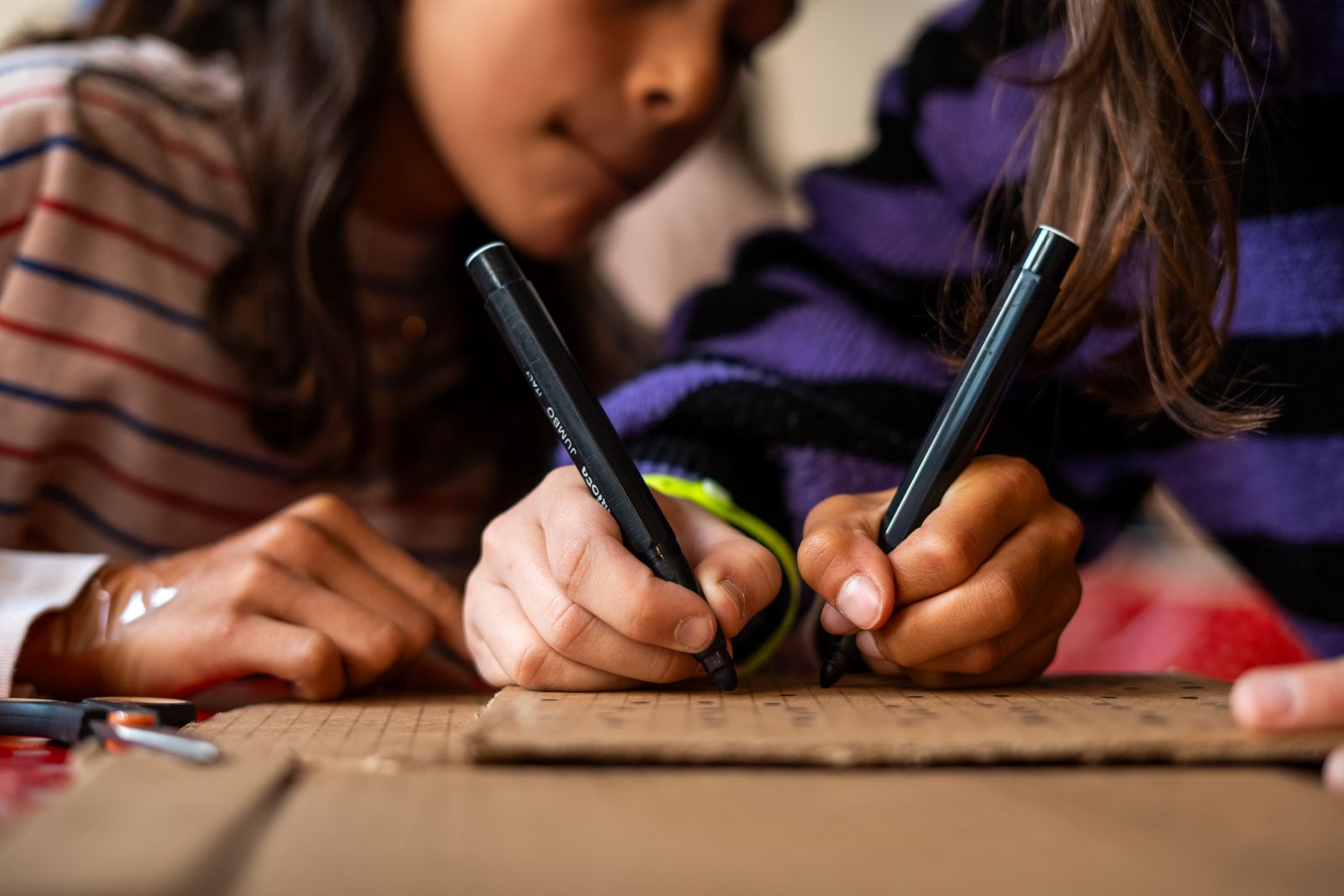 2 meisjes tekenen met zwarte stift op karton