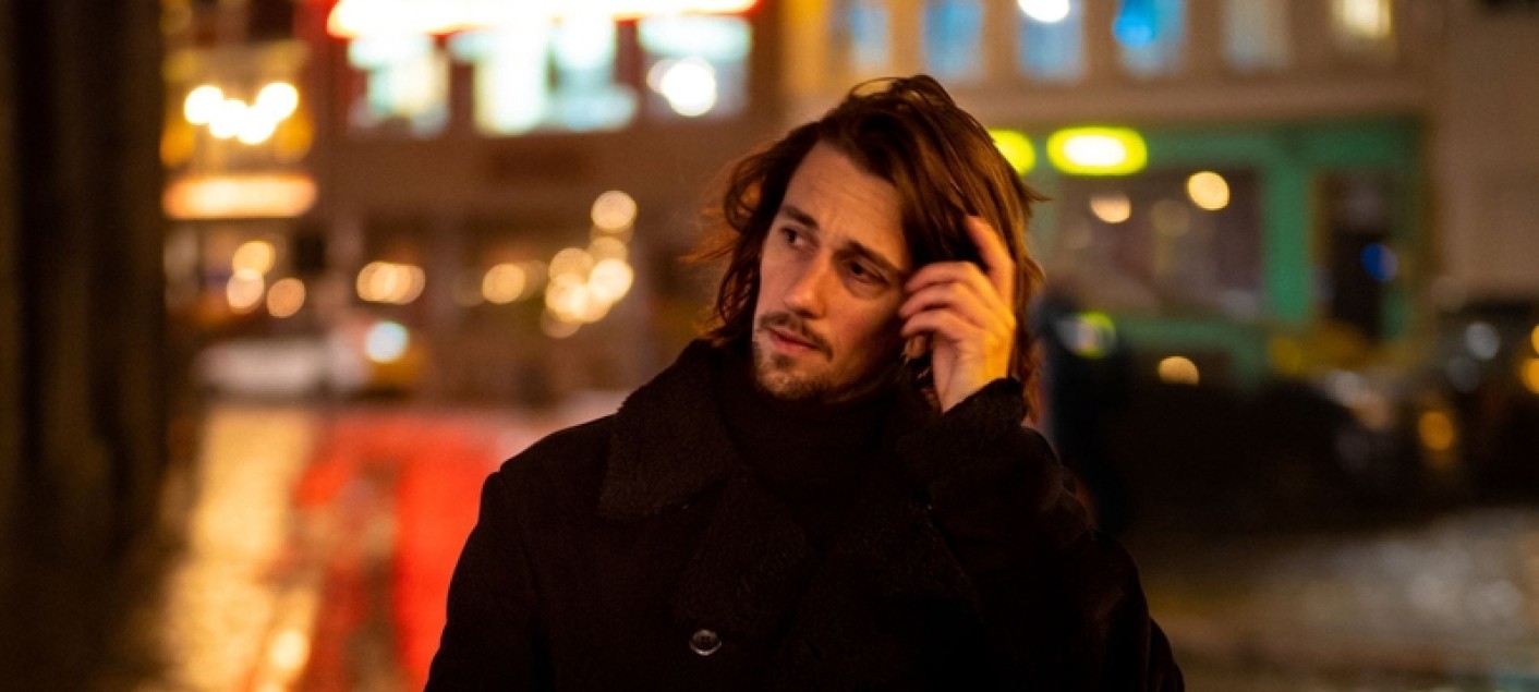 foto van de dichter Jonas Bruyneel, 's avonds of 's nacht in een stad, luisterend met zijn smartphone aan zijn oor