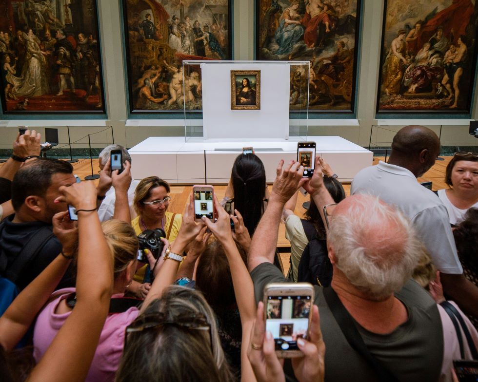 Een massa mensen staat voor het schilderij van de Mona Lisa, allemaal met de gsm in de hand.